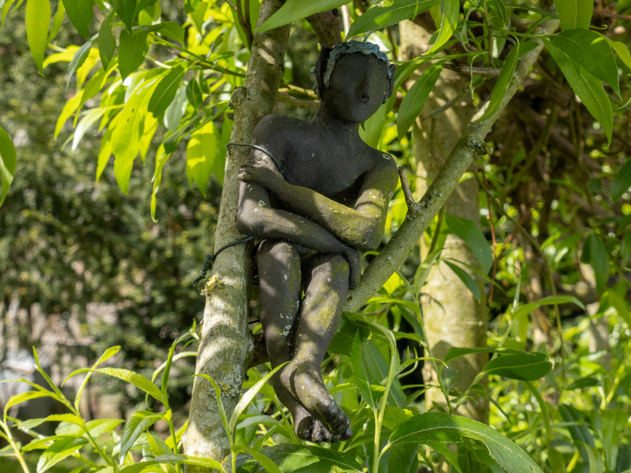 Skulptur eines sitzenden Mannes in einem Busch